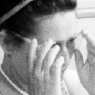 Woman sits near a car, applying cream to her face.