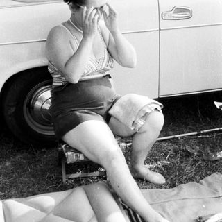 Woman sits near a car, applying cream to her face.