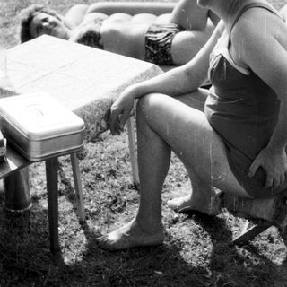 Woman sits near sunbathers on a grassy beach.