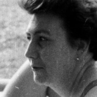 Woman sits near sunbathers on a grassy beach.