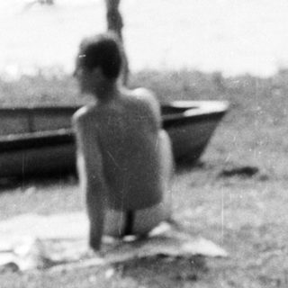 Woman sits near sunbathers on a grassy beach.