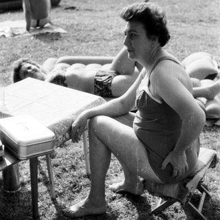 Woman sits near sunbathers on a grassy beach.