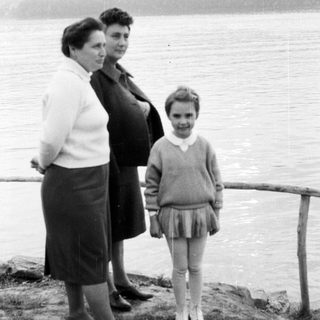 Pregnant woman, another woman, and a young girl by a lake.