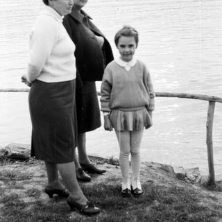 Pregnant woman, another woman, and a young girl by a lake.