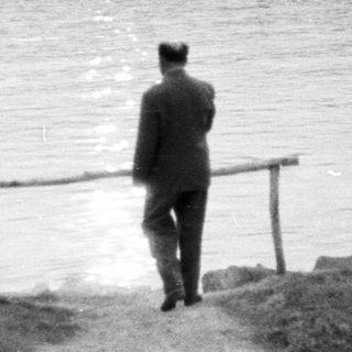 Three figures view a boat across a body of water.
