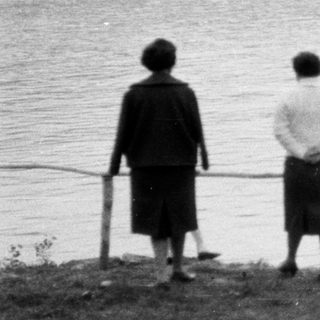 Three figures view a boat across a body of water.