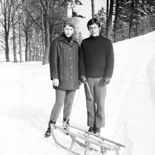 Two people stand near a sled in a snowy landscape.