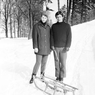 Two people stand near a sled in a snowy landscape.