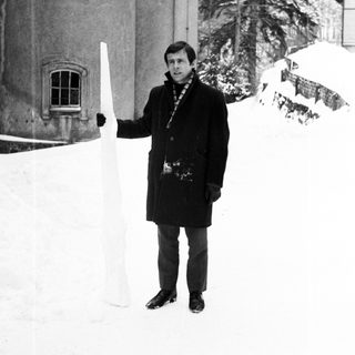 Man stands in snowy landscape next to a snow sculpture.