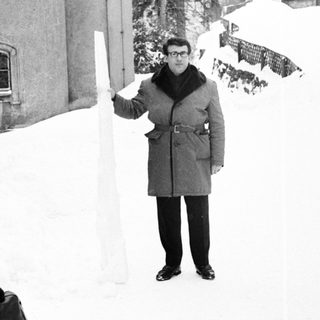 Man in coat holds ice shard in snowy landscape.