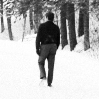 Man walks along a snow-covered path through a forest.
