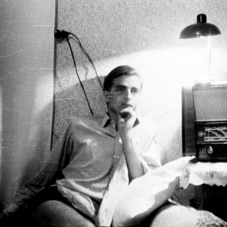 Man seated near vintage radio in a dimly lit room.