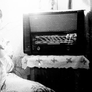 Man seated near a vintage radio, looking towards the camera.