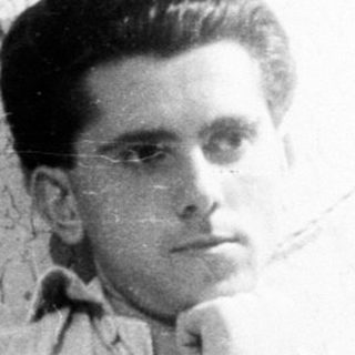 Man seated near a vintage radio, looking towards the camera.