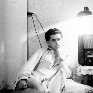 Man seated near a vintage radio, looking towards the camera.