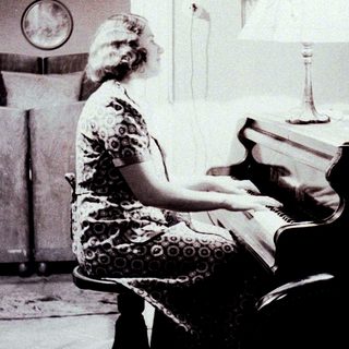 Woman sits at a piano in a vintage-style room.