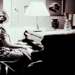 Woman sits at a piano in a vintage-style room.