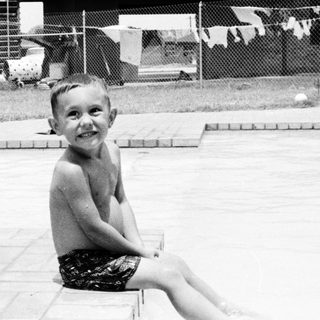 Young boy smiling by empty swimming pool.