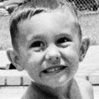 Young boy smiling by empty swimming pool.
