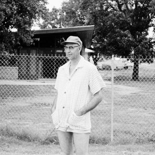 Man in casual 1960s-70s attire standing outdoors near fence.