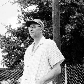 Old man wearing cap and glasses outdoors.