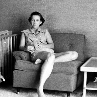 Woman sitting on armchair with baby crib nearby.