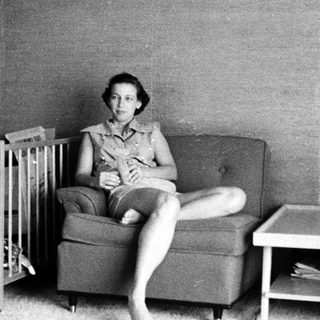 Woman sitting on armchair with baby crib nearby.