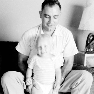 Man holding and comforting a young child indoors.