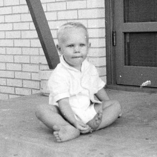 Young child sitting barefoot on concrete near door.