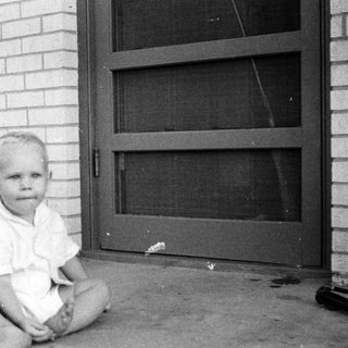 Young child sitting barefoot on concrete near door.
