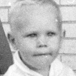Young child sitting barefoot on concrete near door.