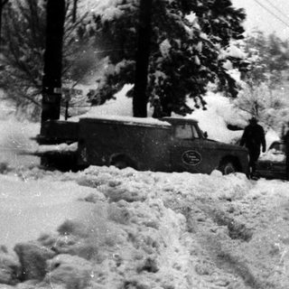 Snow-covered road with stuck vintage vehicles.