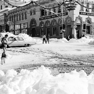 Heavy snowstorm blocks city street and buildings.
