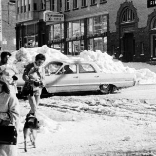 Heavy snowstorm blocks city street and buildings.