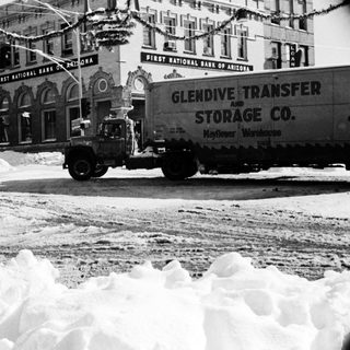Snow-covered city street with truck clearing snow.