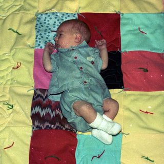 Baby sleeping on colorful patchwork blanket.