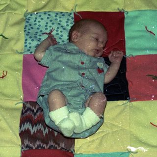 Baby sleeping on colorful patchwork quilt.