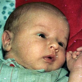 Baby wearing light green onesie, lying on colorful blankets.