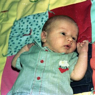 Baby wearing light green onesie, lying on colorful blankets.