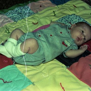 Newborn infant in hospital bassinet with medical tubes.