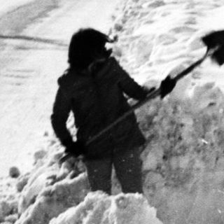Person shoveling heavy snow along a residential road.