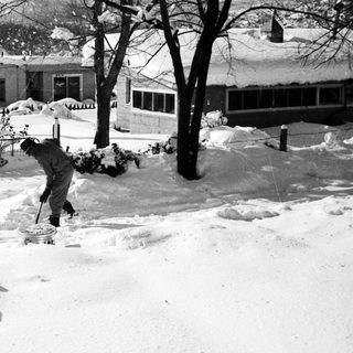 Person shoveling snow-covered residential driveway.