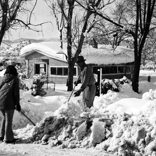 People shoveling heavy snow in a residential area.