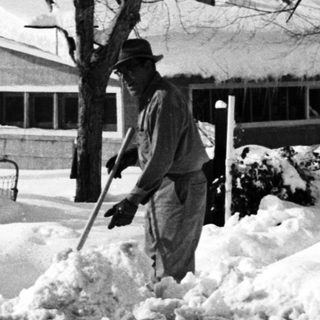 People shoveling heavy snow in a residential area.