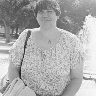 Woman smiling outdoors near park fountain.