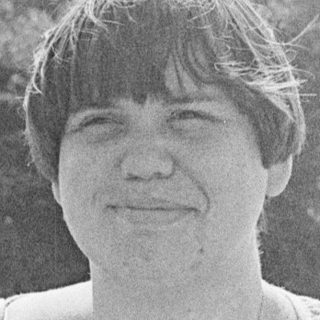 Woman smiling outdoors near park fountain.