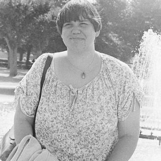 Woman smiling outdoors near park fountain.