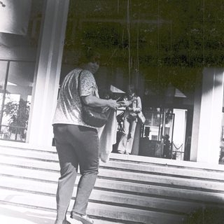 Person holding umbrella outside modern building entrance.