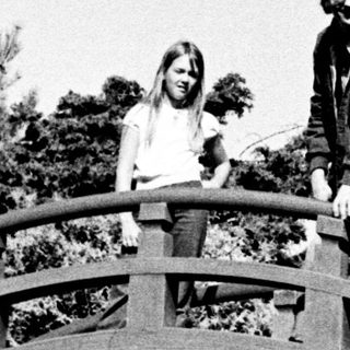 People posing on a curved wooden bridge in a park.