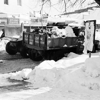 Snow-covered city street with snow truck clearing snow.